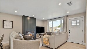 A modern living room with a fireplace, a sofa, a television, and a large window. - Spacious Pacifica Beach Home  Sleeps 14 Game Room (Pacifica)