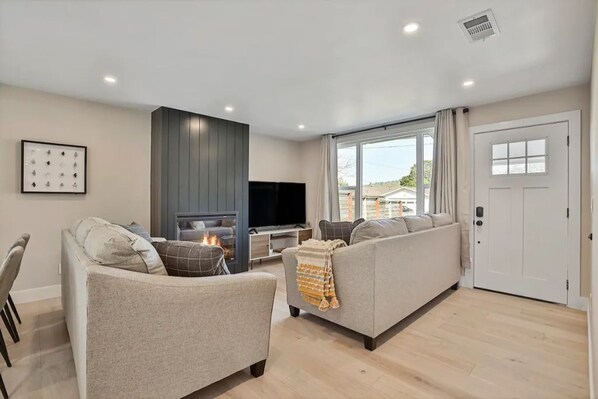 A modern living room with a fireplace, a sofa, a television, and a large window.