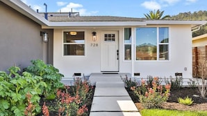 A modern two-story house with a white exterior, numbered 728, featuring a front entrance with a white door and windows, a small porch area, and a well-maintained garden with various plants and flowers. - Spacious Pacifica Beach Home  Sleeps 14 Game Room (Pacifica)