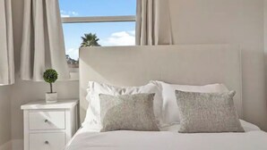 A neatly made bed with two pillows, a small bedside table with a plant, and a window with curtains. - Spacious Pacifica Beach Home  Sleeps 14 Game Room (Pacifica)