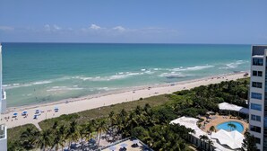 A beach view with a pool area, palm trees, and a clear sky. - 2bd2bth Partial Ocean view Ste w/ balcony, Pool, nearby dining, beach access (Miami Beach)