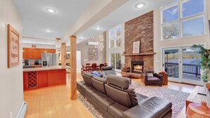 A spacious living area with a fireplace, a large sofa, and a kitchen in the background.
