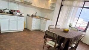 Una cucina compatta con mobili bianchi, un tavolo da pranzo con sedie e vista attraverso un'ampia finestra.