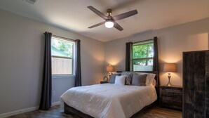 A bedroom with a bed, two bedside tables, a ceiling fan, and windows with curtains.