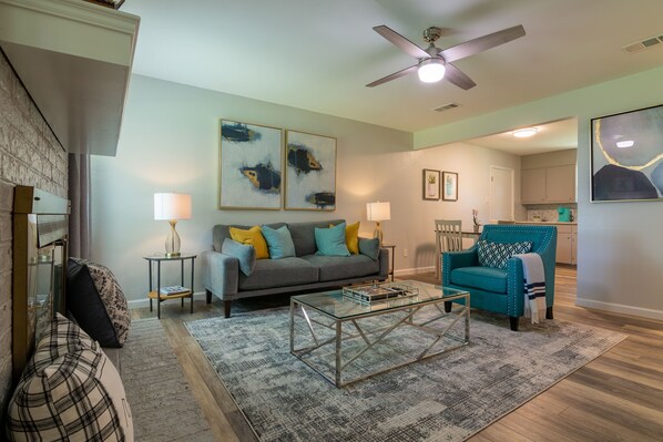 A living room with a sofa, coffee table, and a teal armchair. There are two paintings on the wall and a ceiling fan. - Quiet & Cozy in Georgetown, TX-Pets-Long Stays-Office (Georgetown)