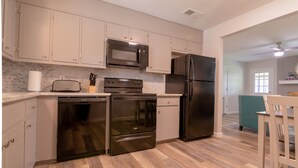 A modern kitchen with stainless steel appliances, light-colored cabinets, and a wooden floor.