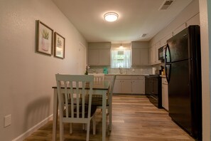 Une cuisine avec un plancher en bois, une table à manger avec des chaises, un réfrigérateur et un four à micro-ondes.