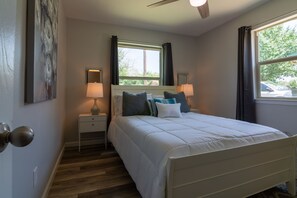 A bedroom with a bed, bedside lamps, a window with curtains, a nightstand, and a door with a round handle. - Quiet & Cozy in Georgetown, TX-Pets-Long Stays-Office (Georgetown)