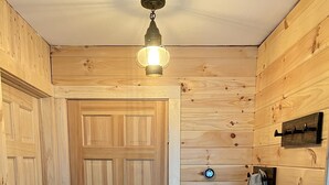 Un pasillo revestido de madera con una puerta, una lámpara, un perchero y un enchufe.
