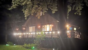 Una cabaña de madera con porche, rodeada de árboles e iluminada con luces colgantes.