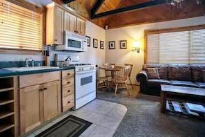 A compact kitchen with wooden cabinets, a stove, and a dining area with a table and chairs. - Serene retreat is just steps to the National Forest (Big Bear)