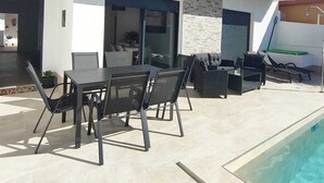 A modern outdoor patio with a pool, a dining area with chairs and a table, and a covered seating area with cushions. - Independent villa with private pool, 5 min from the beach! (San pedro del Pinatar)
