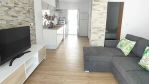 A modern living room with a flat-screen TV, grey sofa, and a kitchen area in the background. - Independent villa with private pool, 5 min from the beach! (San pedro del Pinatar)