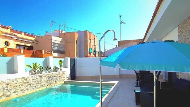 An outdoor swimming pool with a blue umbrella, lounge chairs, and a stone wall. - Independent villa with private pool, 5 min from the beach! (San pedro del Pinatar)