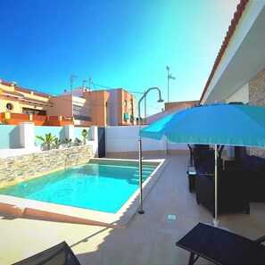 An outdoor swimming pool with a blue umbrella, lounge chairs, and a stone wall. - Independent villa with private pool, 5 min from the beach! (San pedro del Pinatar)