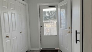 A hallway with white doors, a light switch, and a vent on the ceiling.