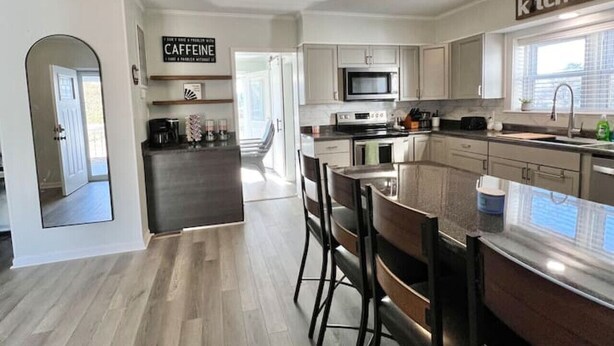 A modern kitchen with a central island, a dining area with chairs, and a sign that reads "CAFFEINE".