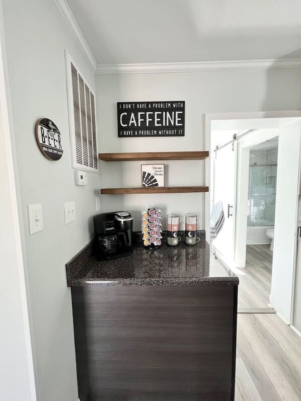 Una cocina con cafetera, tazas y un cartel en la pared.