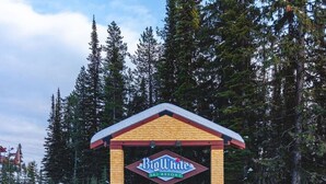 A Big White Ski Resort sign with a red roof and yellow brick base, surrounded by snow and trees. - The Fjäll | Ski-In Ski-Out Village Studio (Big White)