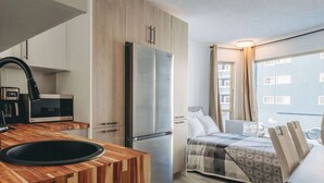 A compact kitchen with modern appliances, a wooden countertop, and a bed with a checkered blanket. - The Fjäll | Ski-In Ski-Out Village Studio (Big White)