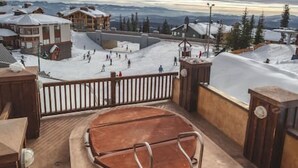 A snowy outdoor area with a wooden deck and metal railings, surrounded by buildings and trees. - The Fjäll | Ski-In Ski-Out Village Studio (Big White)