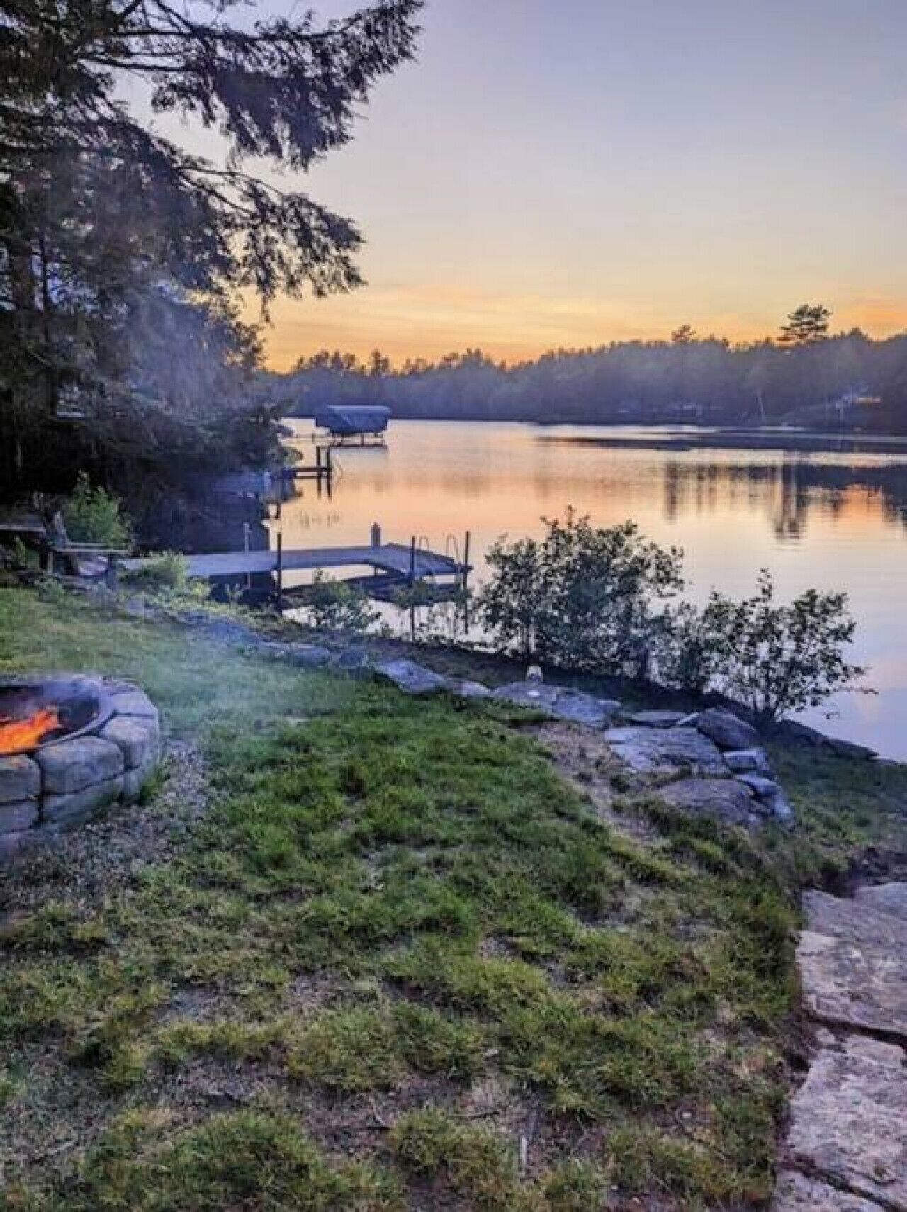 A lakeside property with a dock, a fire pit, and a grassy area.