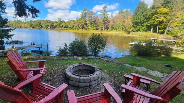 A lakeside setting with a fire pit and Adirondack chairs.