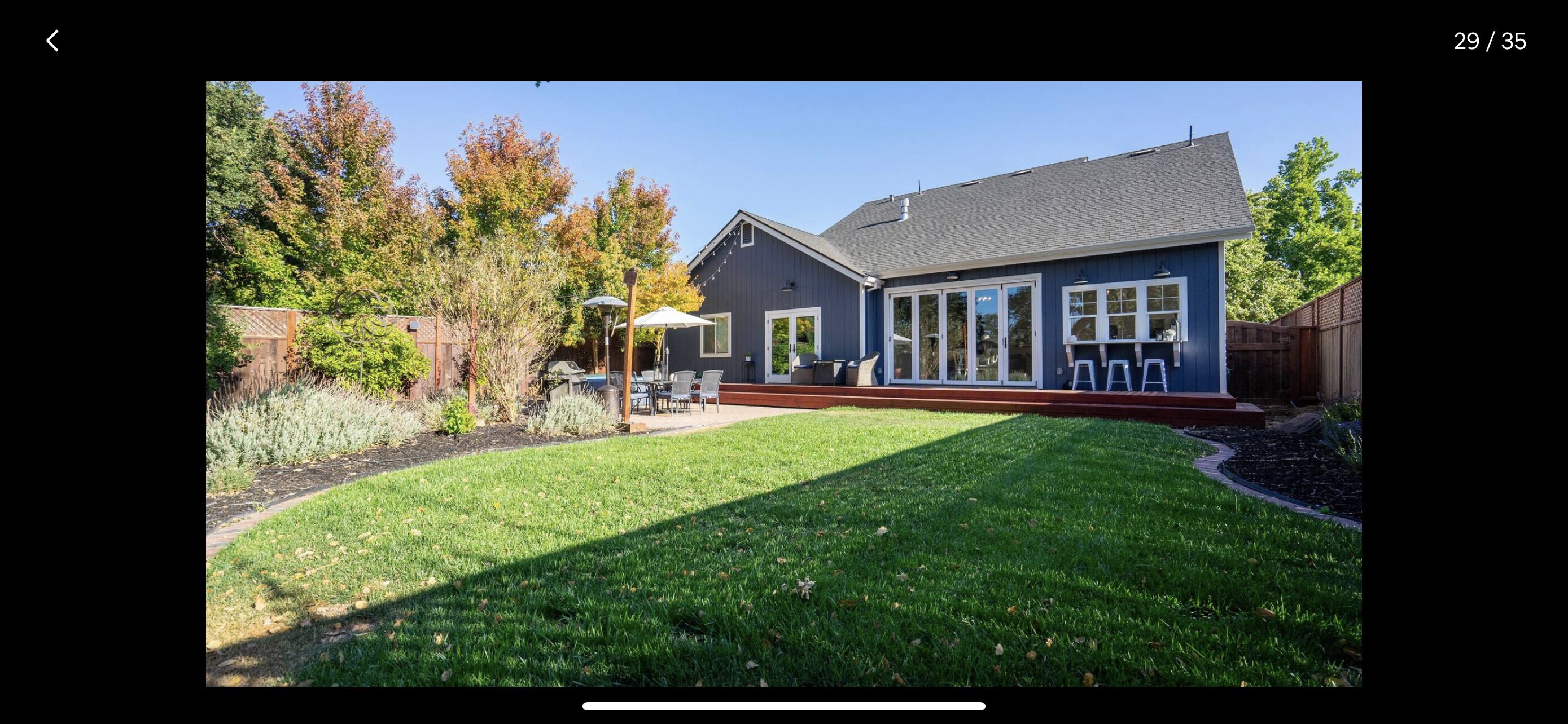 Une maison d’habitation avec une pelouse bien entretenue, une terrasse dotée de meubles d’extérieur et une grande porte-fenêtre coulissante.