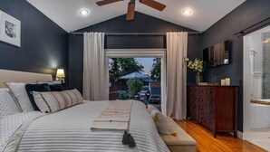 Ein Schlafzimmer mit einem großen Bett, Deckenventilator, Fernseher, Kommode und Blick ins Freie.