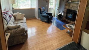A cozy living room with a wooden floor, a sofa, a recliner, a fireplace, and a television. - Cozy & Private Upper Michigan Riverfront Cottage With 970 ft. Of River Frontage! (Republic)