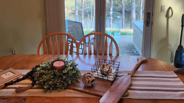 A dining table with chairs, a chandelier, and a view of a forest through a glass door. - Cozy & Private Upper Michigan Riverfront Cottage With 970 ft. Of River Frontage! (Republic)
