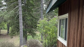 A wooden cabin with a window, surrounded by a forested area and a concrete patio. - Cozy & Private Upper Michigan Riverfront Cottage With 970 ft. Of River Frontage! (Republic)