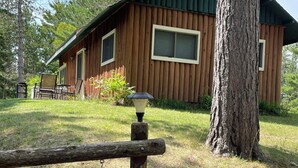 A wooden cabin with a porch, a welcome sign, and a Christmas tree decoration. - Cozy & Private Upper Michigan Riverfront Cottage With 970 ft. Of River Frontage! (Republic)