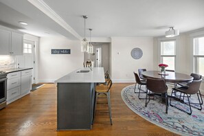 Una cocina moderna con armarios blancos, una isla central y una zona de comedor con una mesa redonda y sillas.