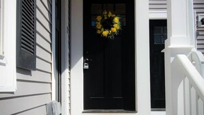 A front porch with a black door, a yellow wreath, and a doormat. - Stunning Home Mins to Boston w/Parking & Laundry (Somerville)