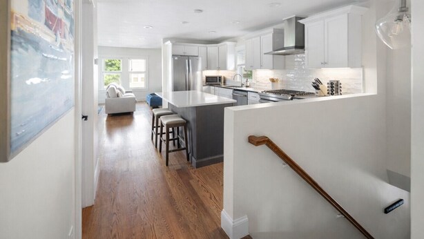 A modern kitchen with white cabinets, a central island, and a dining area with a sofa and chairs. - Stunning Home Mins to Boston w/Parking & Laundry (Somerville)