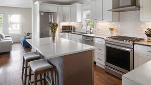 A modern kitchen with white cabinetry, stainless steel appliances, and a central island with bar stools. - Stunning Home Mins to Boston w/Parking & Laundry (Somerville)