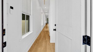 Un couloir aux murs blancs, doté d’un plancher en bois et agrémenté d’un lustre.