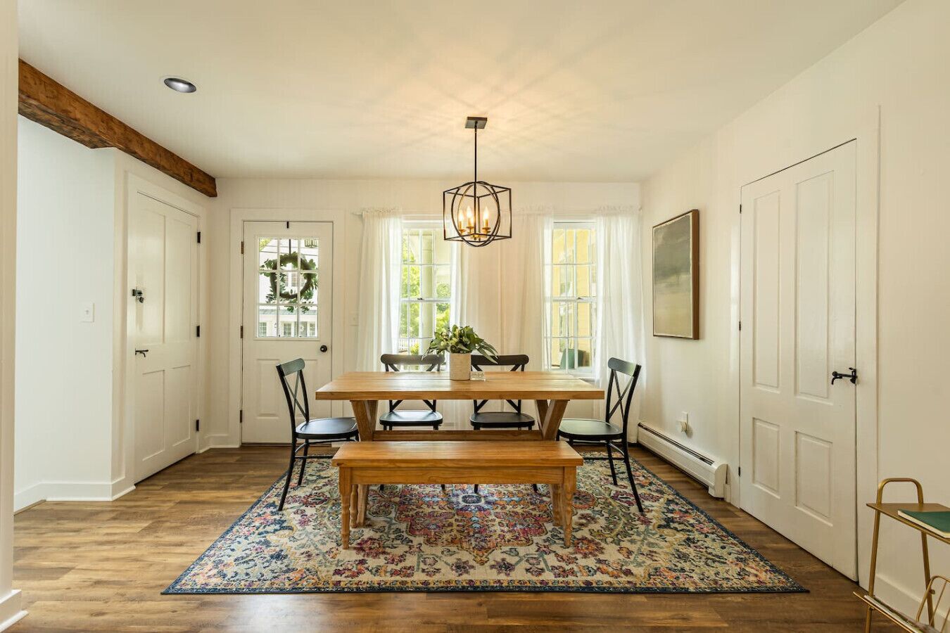 Uma sala de jantar com mesa de madeira, quatro cadeiras, um banco, um candelabro e um tapete estampado.