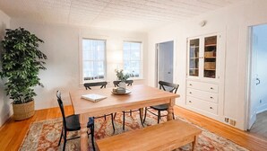 Una habitación amplia con una mesa de madera, sillas, un banco y una planta grande en maceta.