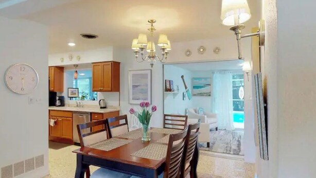 A dining area with a wooden table and chairs, a vase with flowers, and a chandelier.