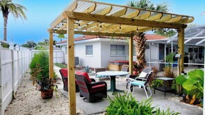 A covered patio area with outdoor furniture, a barbecue, and potted plants.