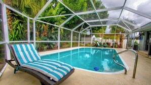 A covered swimming pool with a lounge chair and a poolside table.