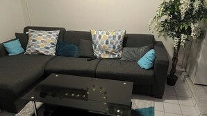 A living room with a sectional sofa, patterned cushions, a glass coffee table, and a potted plant.