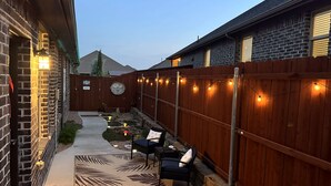 A backyard with a wooden fence, a patio with chairs, and string lights.