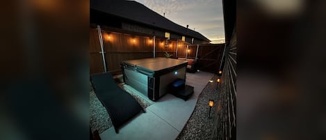 An outdoor hot tub area with a wooden deck, a covered seating area, and string lights.