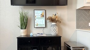 A black console table with a framed welcome sign, a potted plant, a decorative vase, and a small stack of papers.