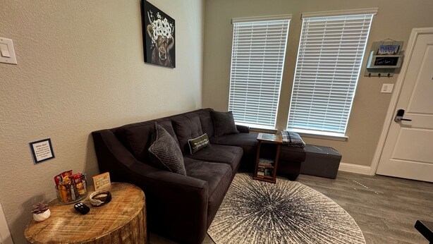 A living room with a dark brown sofa, a round rug, and a small wooden side table with snacks.