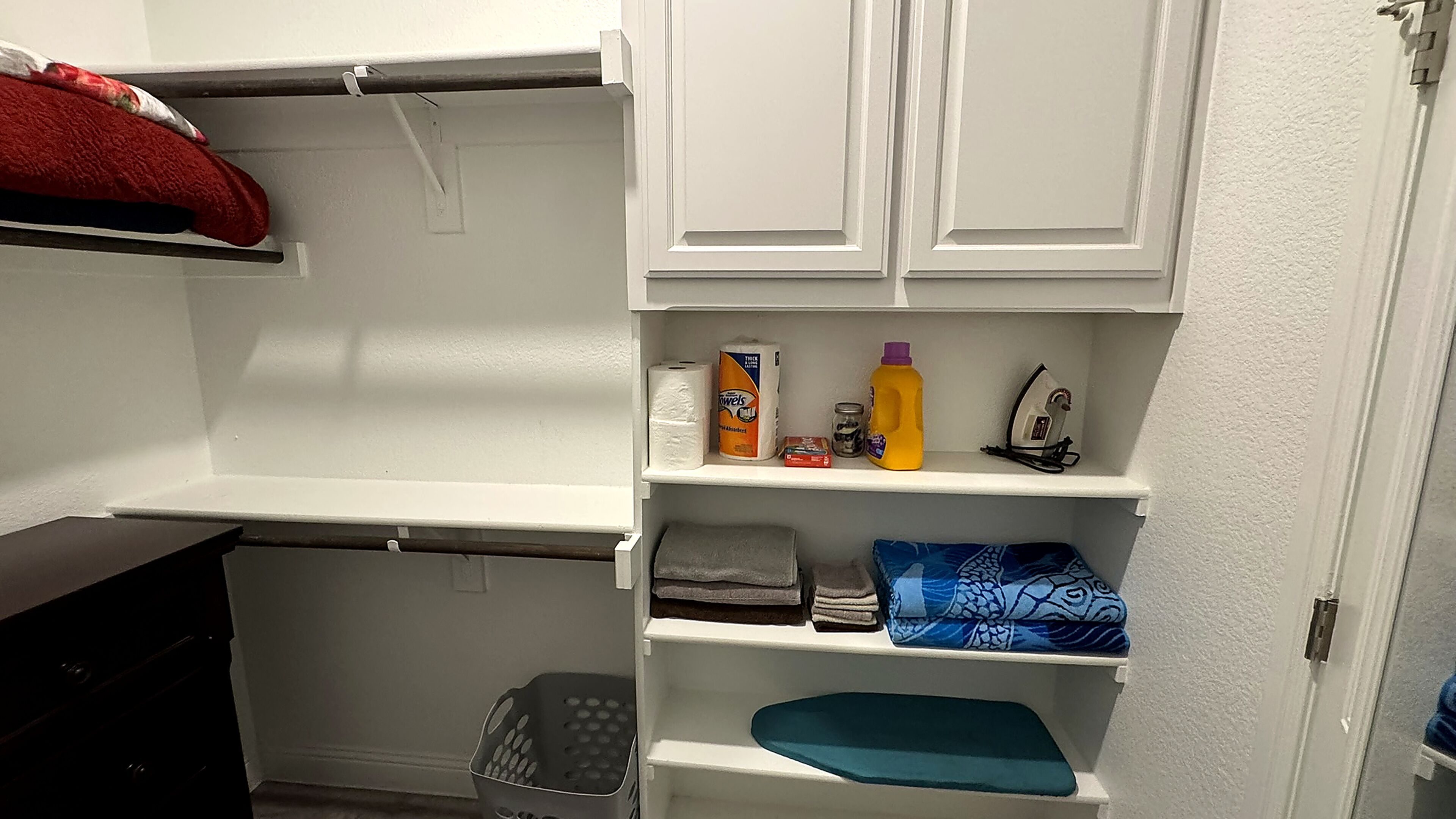 A storage closet with shelves containing towels, cleaning supplies, and a basket.