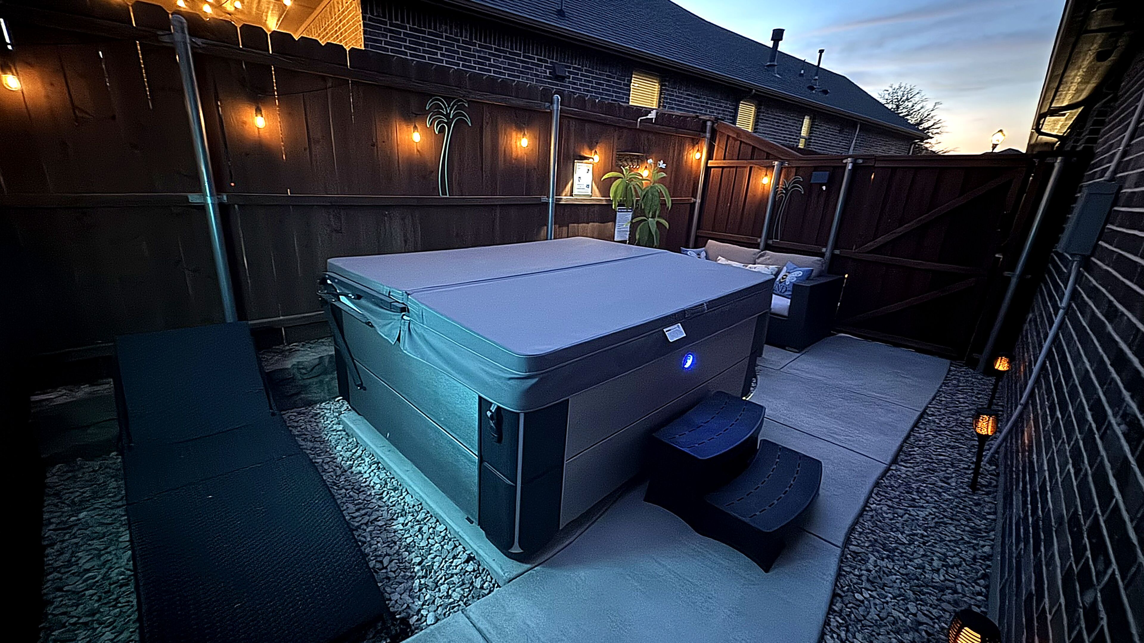 A hot tub in an outdoor setting with a wooden fence and string lights.